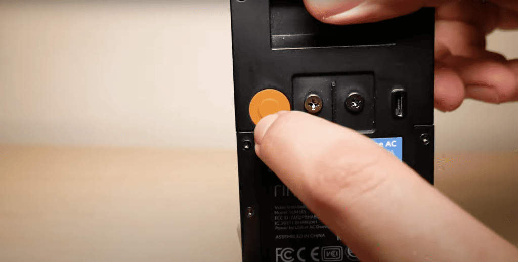 Pointing at the orange button at the back of the Ring doorbell